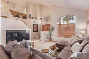 Amplia sala de estar con un sofá modular grande, un televisor de pantalla plana, una escalera y un ventanal con persianas.
