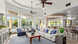 A spacious living room with a large sectional sofa, a coffee table, and a patterned rug. There are ceiling fans, large windows, and a view of the outdoors. - Recker #73 Mesa (Mesa)
