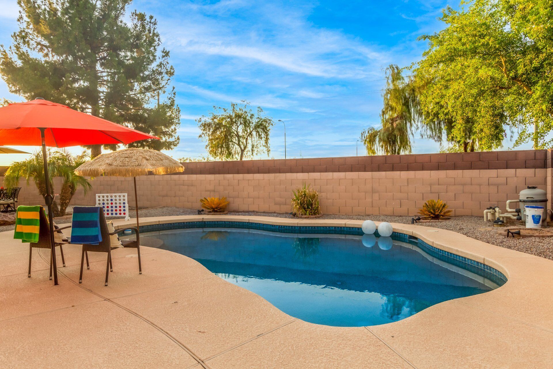 A swimming pool with a brick wall, lounge chairs, and a thatched umbrella.