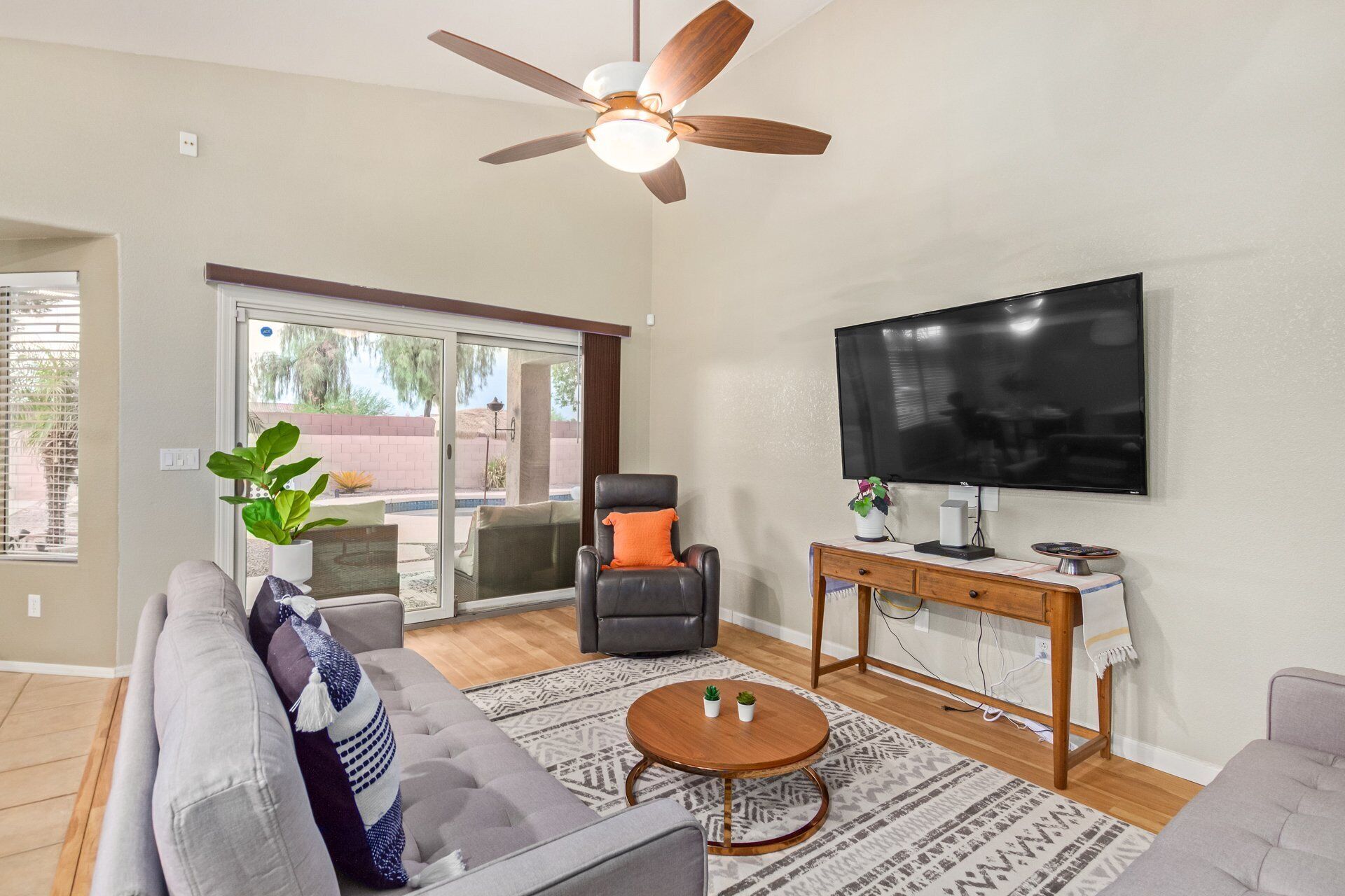 A living room with a sofa, armchair, coffee table, TV, and ceiling fan.