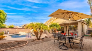 Un patio con piscina, mobiliario exterior y una pérgola con sombrilla.