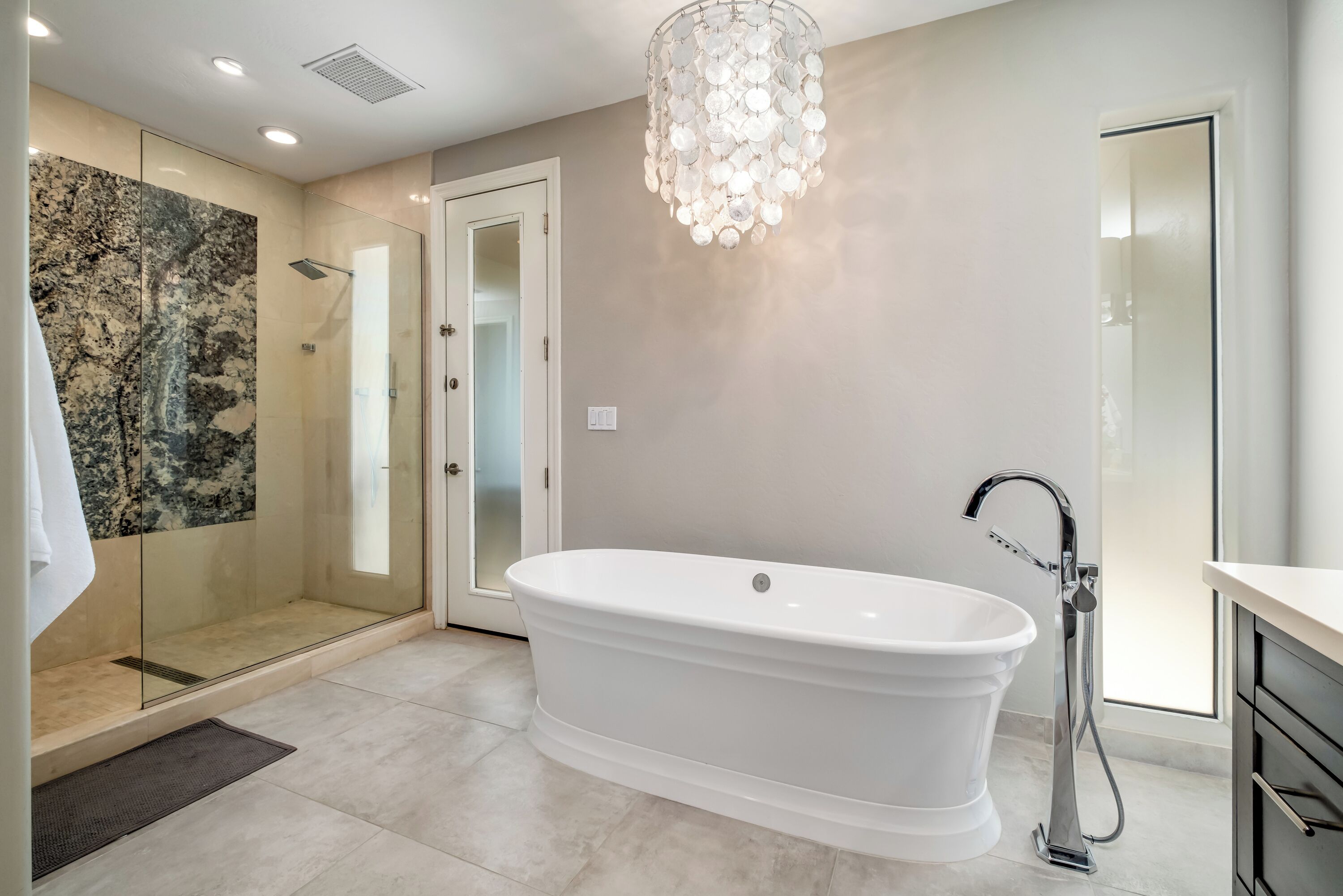 Une salle de bain moderne avec une baignoire sur pieds, une douche à parois de verre et un lustre.
