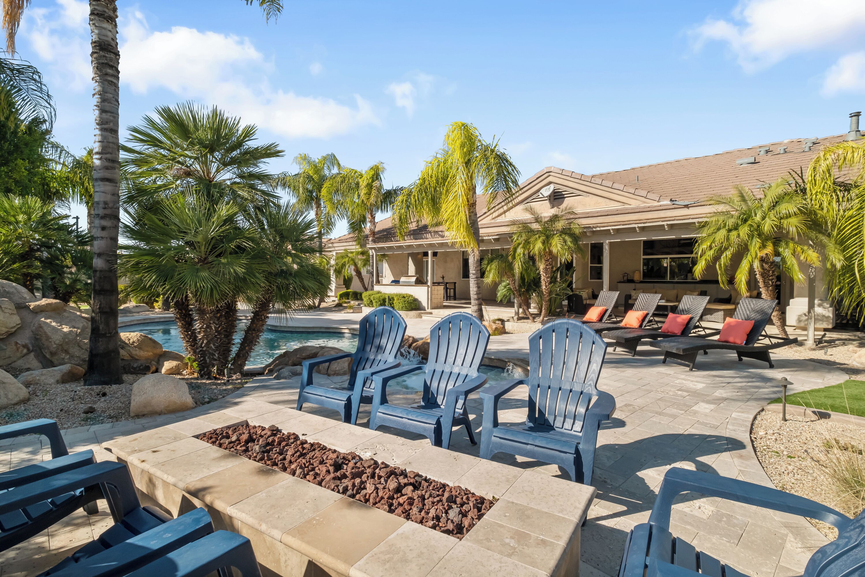 Un espace aménagé au bord de la piscine, avec des chaises Adirondack bleues, un foyer et une piscine.