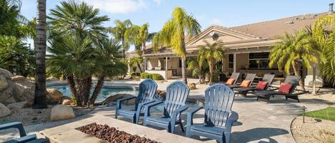 Un espace aménagé au bord de la piscine, avec des chaises Adirondack bleues, un foyer et une piscine.