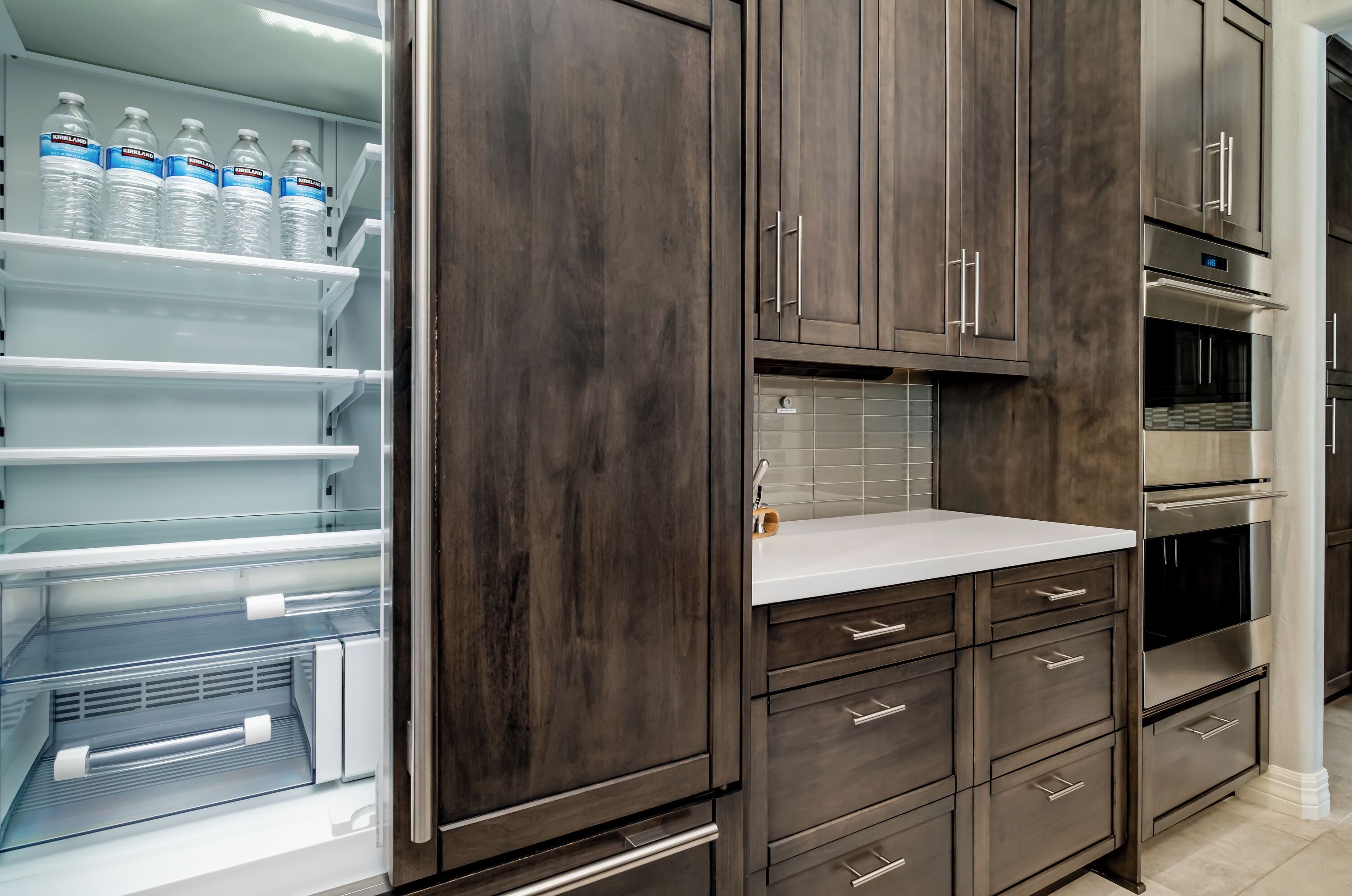Una cocina moderna con armarios de madera oscura, electrodomésticos de acero inoxidable y encimera blanca.