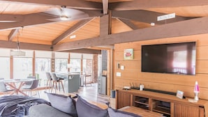 Un amplio espacio de estar con una gran televisión de pantalla plana, vigas de madera, un ventilador de techo y un letrero que dice "The Classic House".