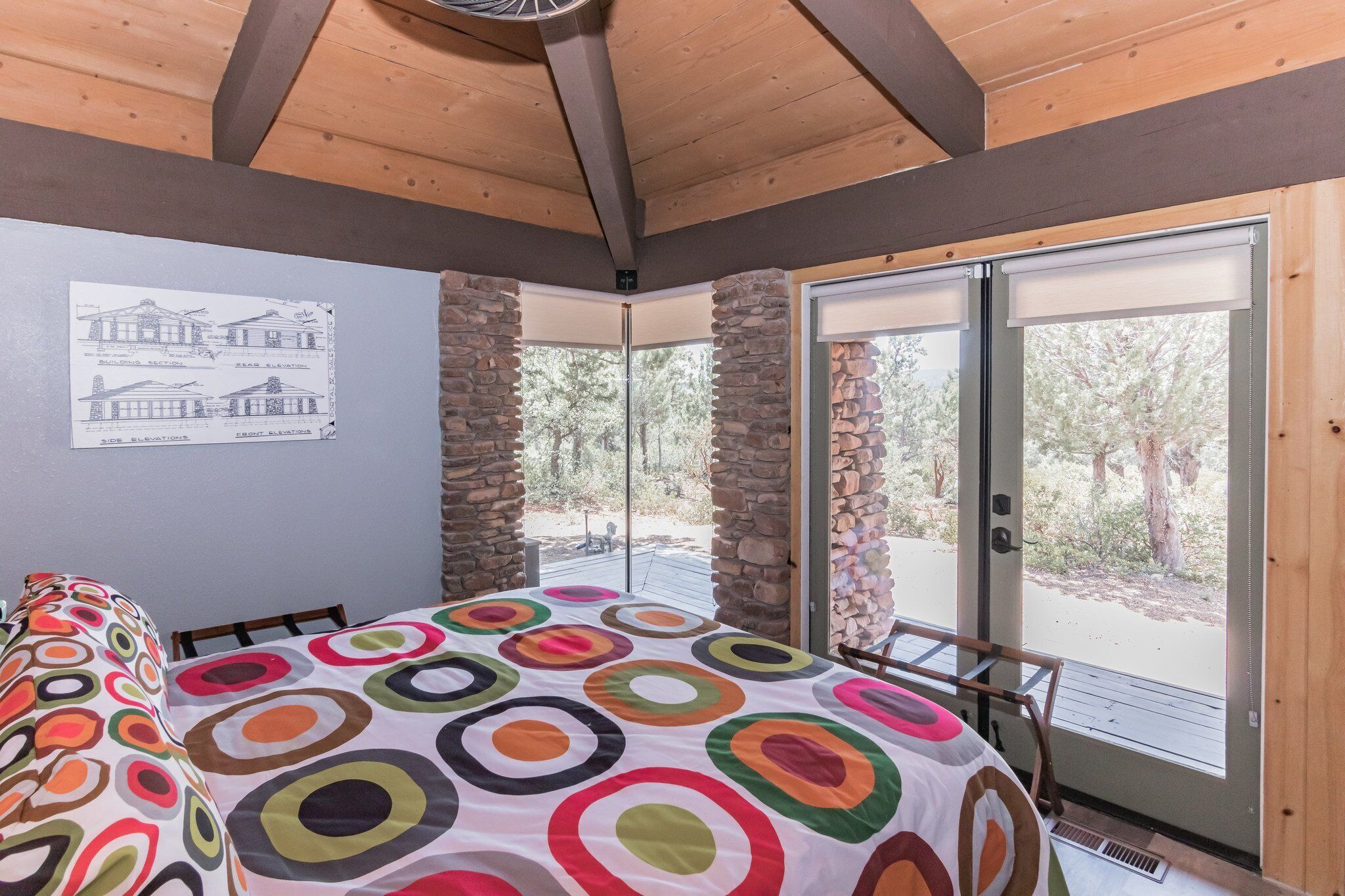 Una habitación con una cama, un ventanal con vista a árboles y una pared con un plano.