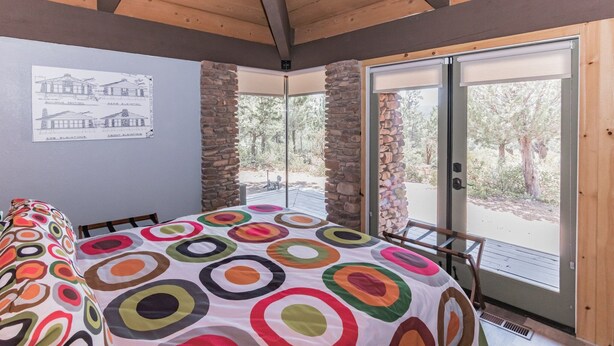 Una habitación con una cama, un ventanal con vista a árboles y una pared con un plano.