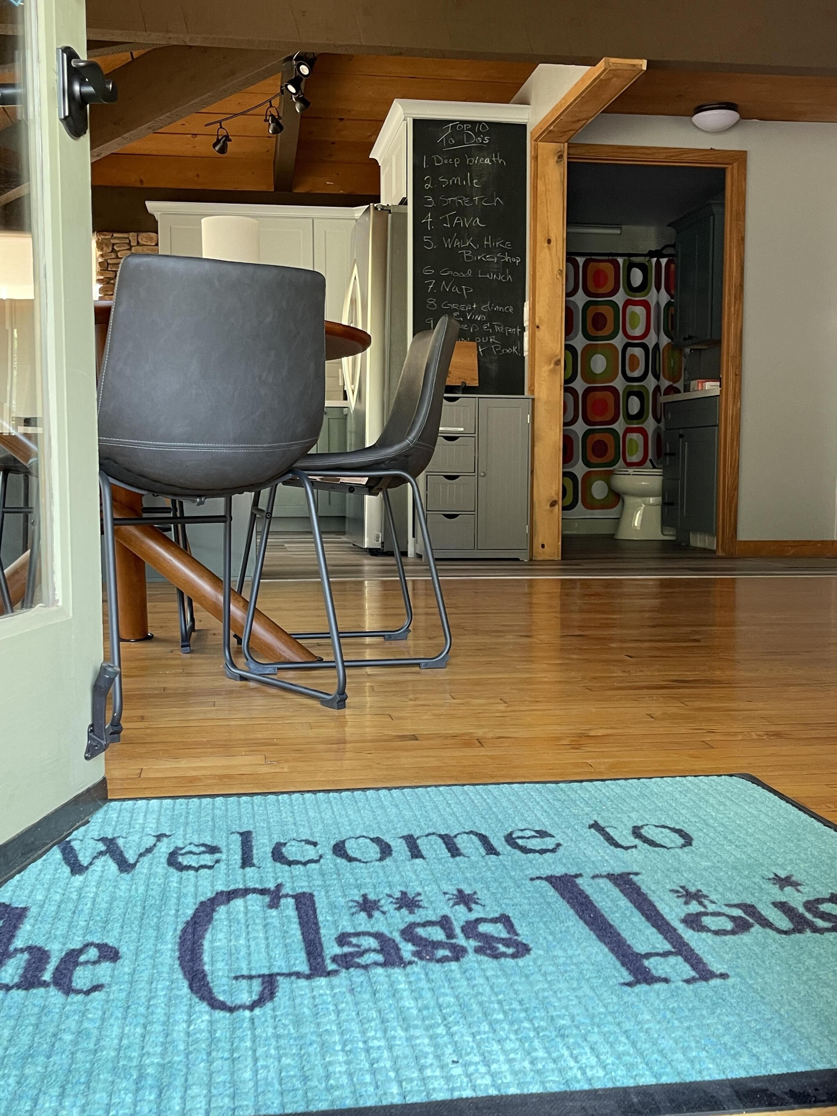 A classroom with a wooden floor, a blackboard with a list, and a welcome mat.