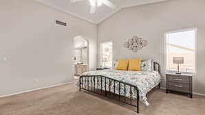 A bedroom with a bed, a nightstand, a wall-mounted lamp, a ceiling fan, and a window with blinds. - Emile Zola Peoria (Peoria)