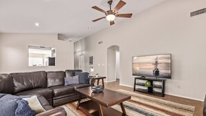 A modern living room with a leather sofa, a wooden coffee table, a ceiling fan, and a TV on a black stand. - Emile Zola Peoria (Peoria)