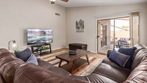 A living room with a brown leather sofa, a wooden coffee table, a TV on the wall, and a ceiling fan. - Emile Zola Peoria (Peoria)