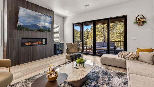 A modern living room with a fireplace, comfortable seating, and a large window with a view of trees. - Cottonrose Flagstaff (Flagstaff)