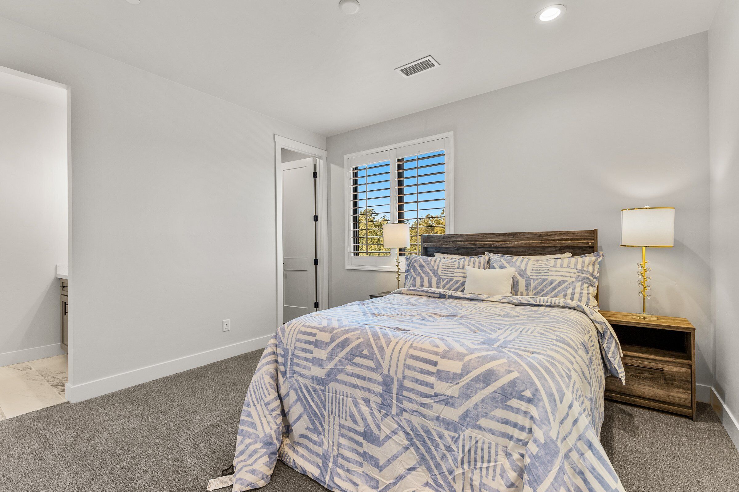 A bedroom with a bed, bedside tables, a lamp, and a window with blinds.