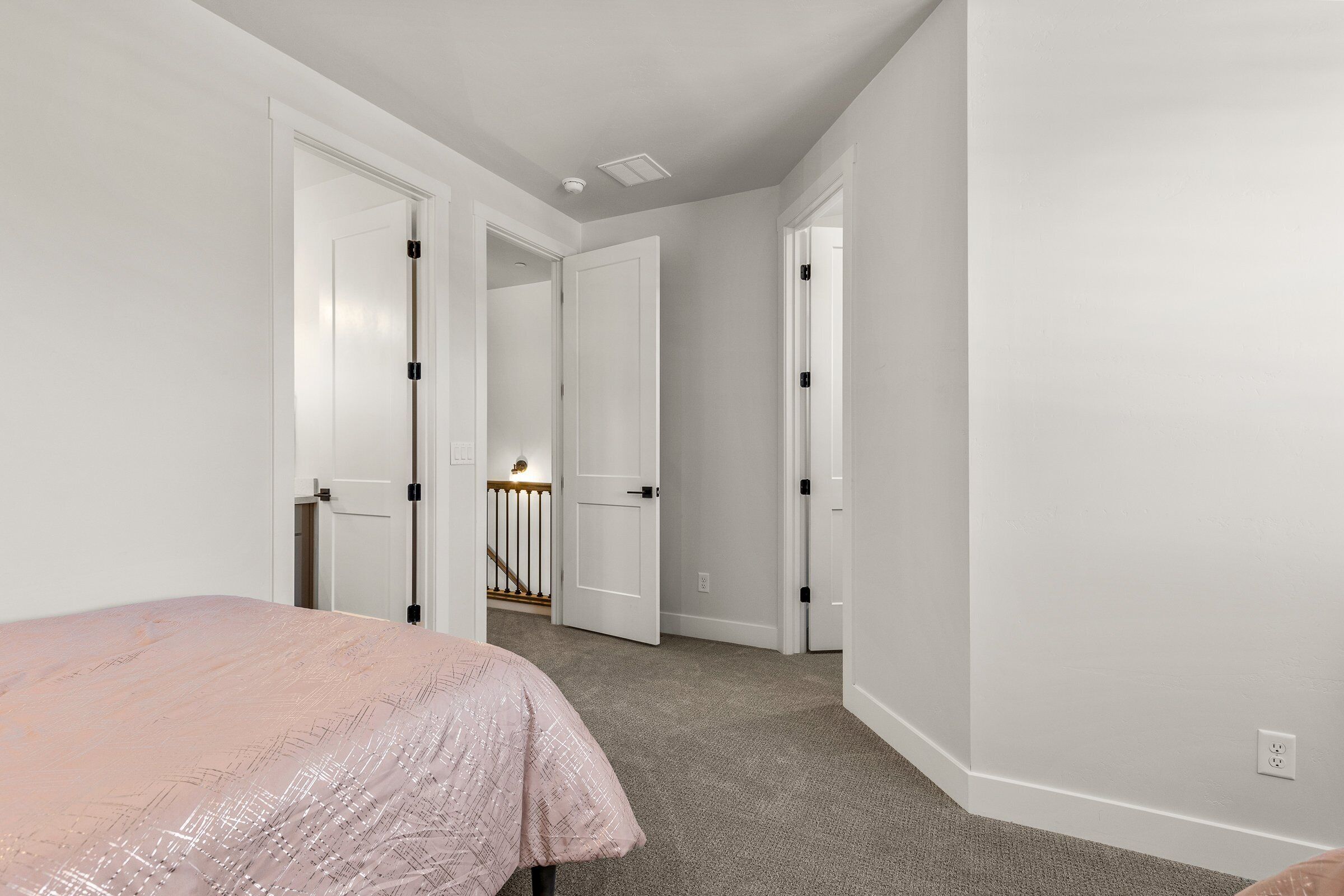 Een slaapkamer met een bed, vloerbedekking, witte muren en een deur naar een trap.