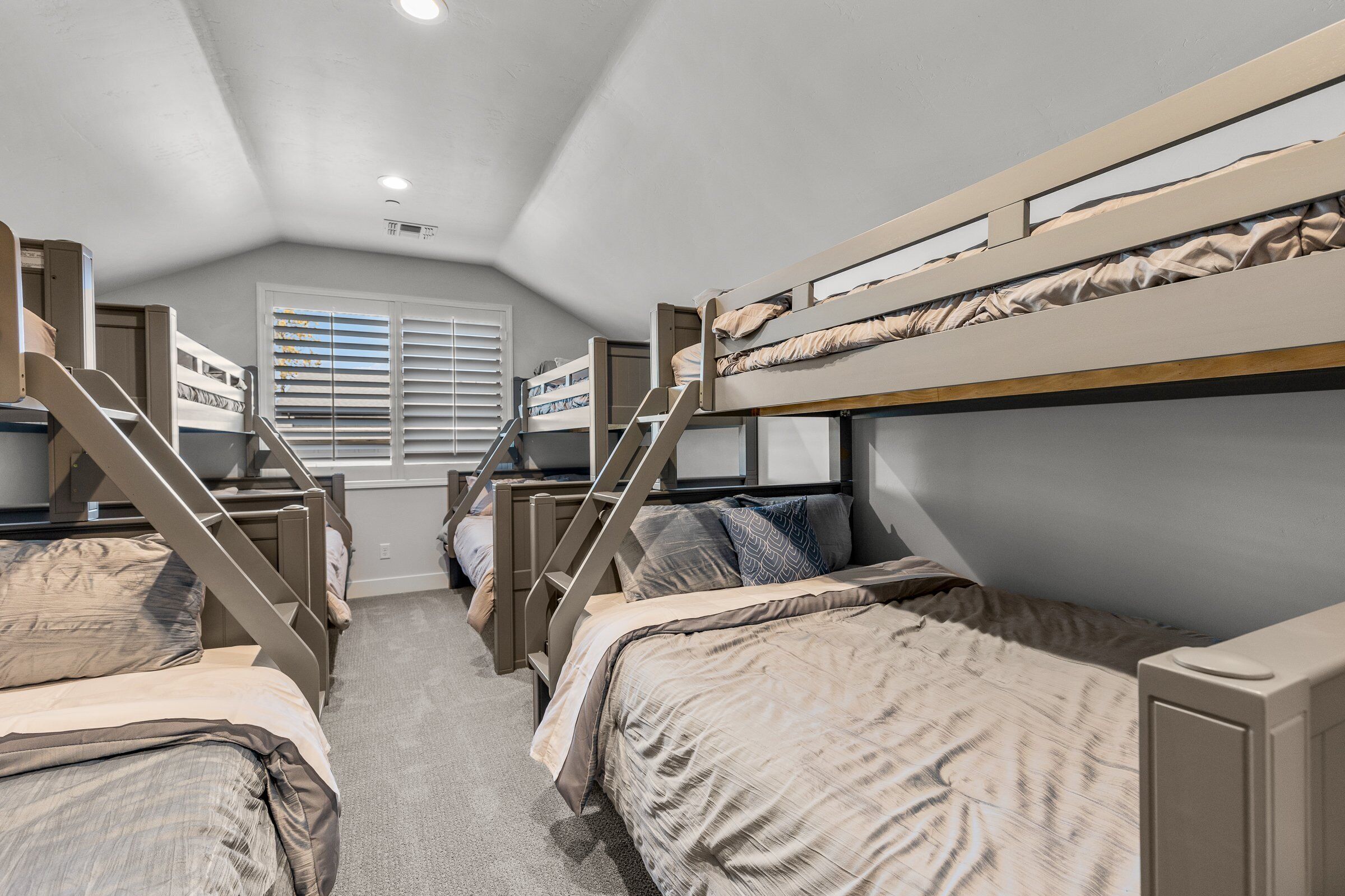 A dormitory room with bunk beds, a staircase, and a window with blinds.
