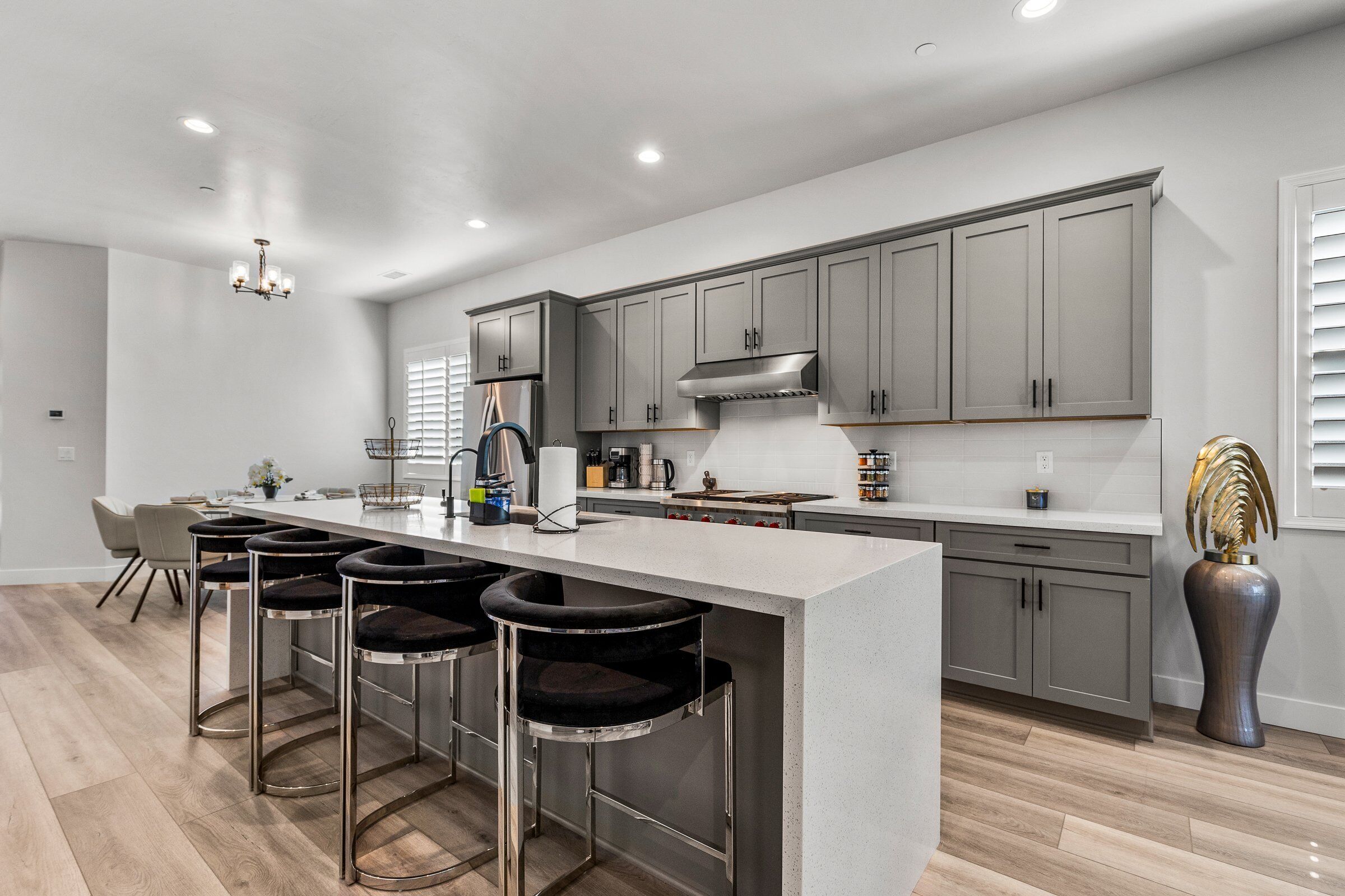 A modern kitchen with a large island, bar stools, and grey cabinetry.