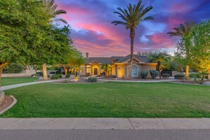 A residential house with a well-maintained lawn, a driveway, and a large palm tree.