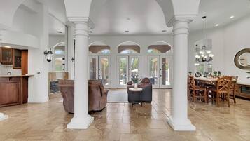 A spacious interior with high ceilings, white columns, a dining area, and a kitchen.