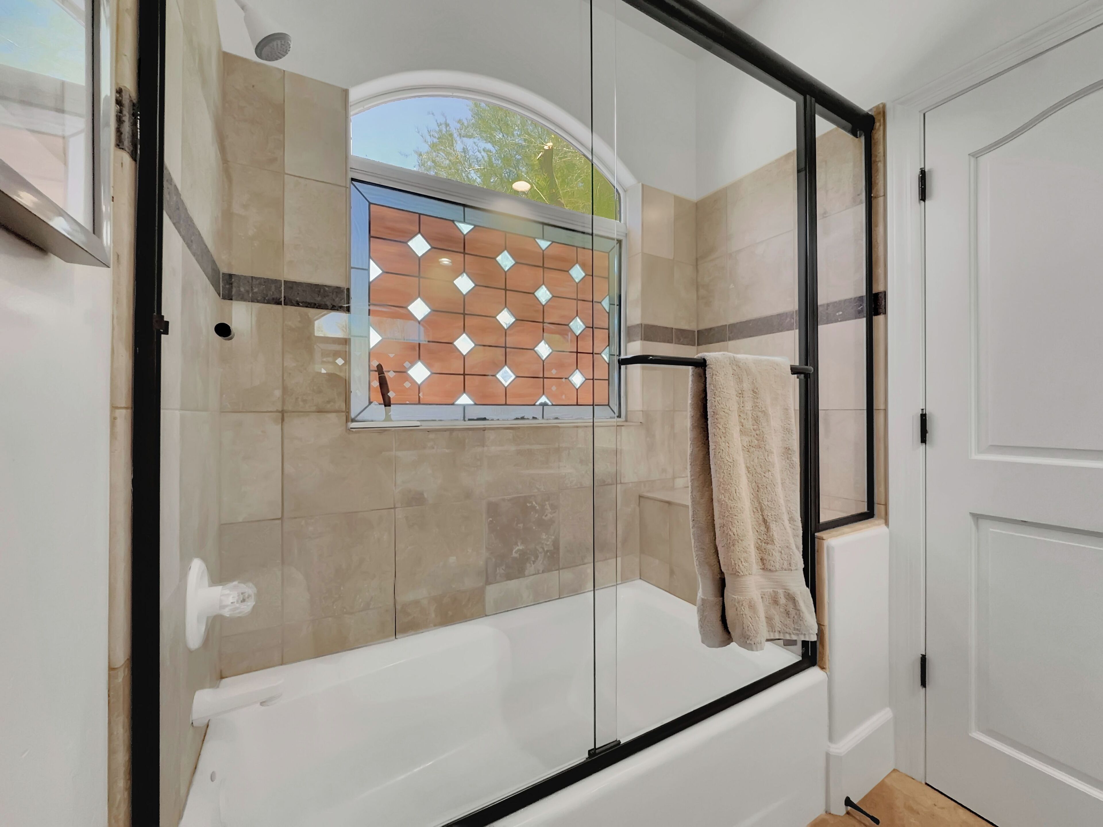 Een moderne badkamer met een douchecabine van glas, een wit bad en een raam met een diamantpatroon van tegels.