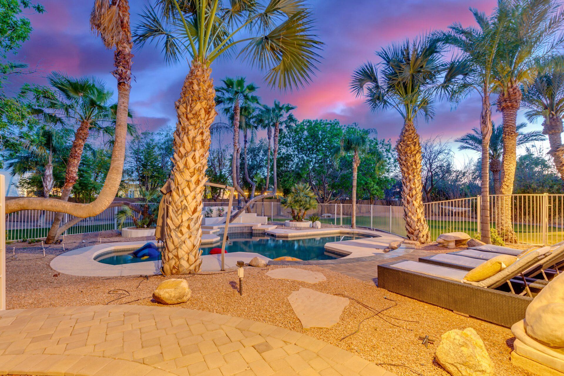 A pool area with palm trees, a hot tub, and a lounge chair.