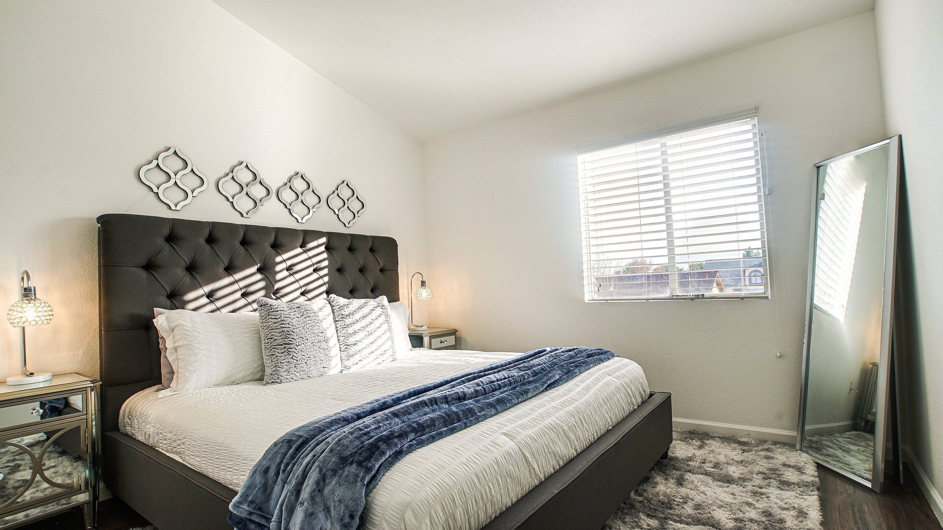 A bedroom with a large bed, a nightstand, a mirror, and a window with blinds.