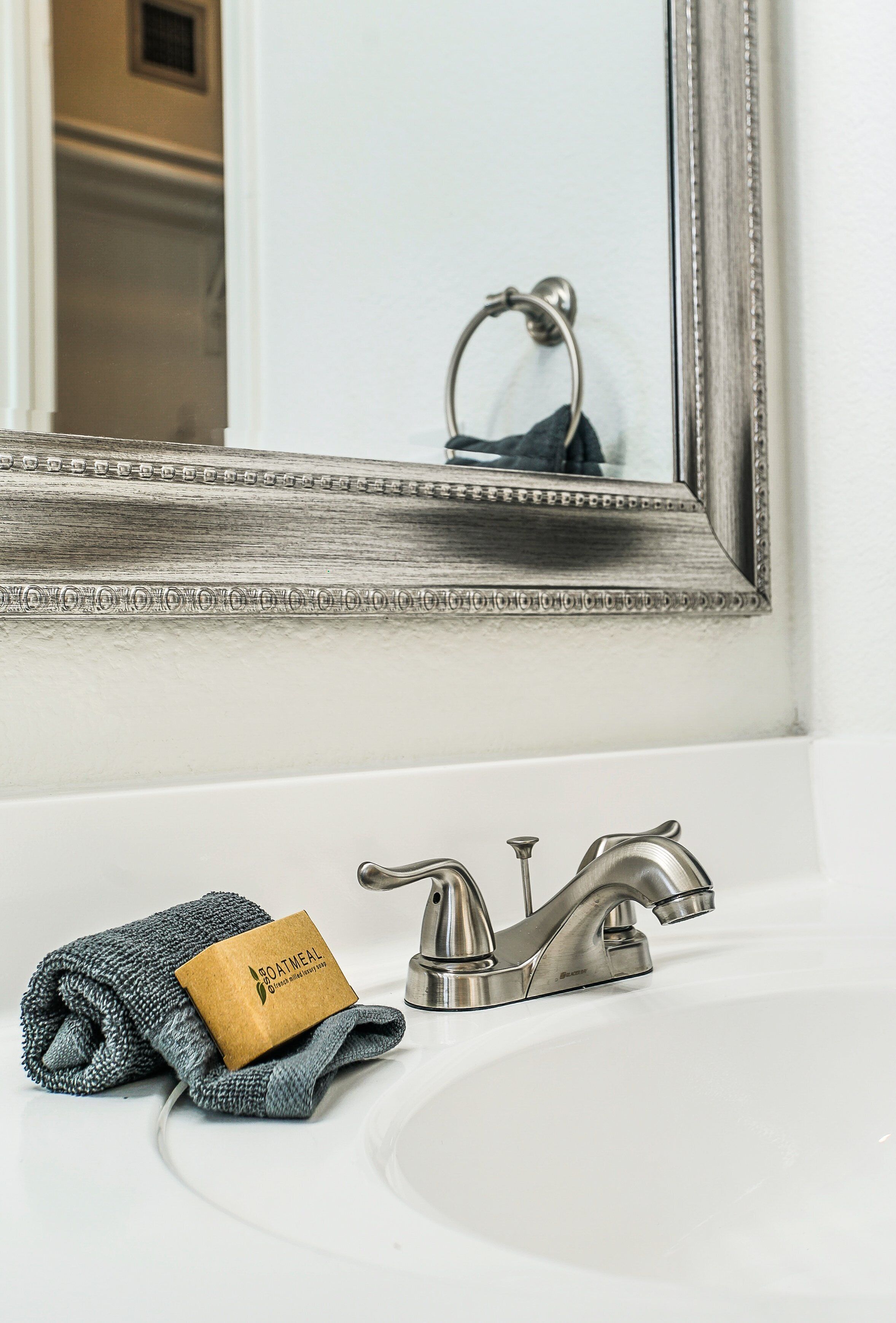 A bathroom with a white sink, a silver faucet, and a mirror with a decorative frame.