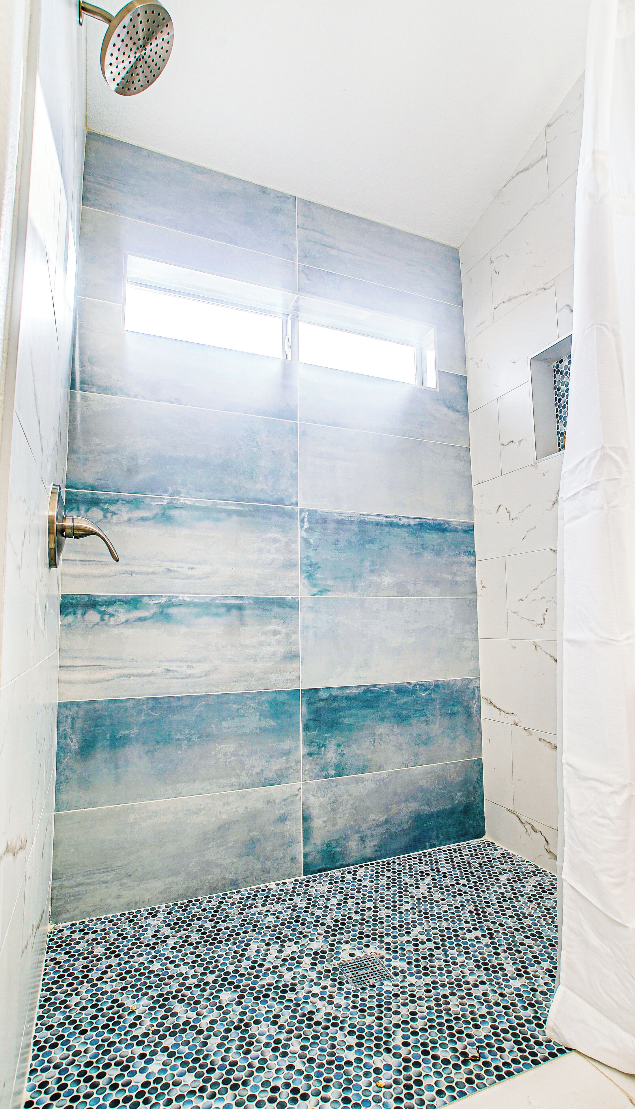 Ducha con azulejos azules y blancos y suelo de mosaico.
