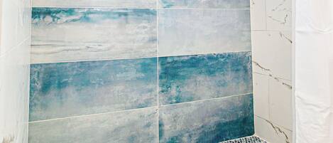 Ducha con azulejos azules y blancos y suelo de mosaico.