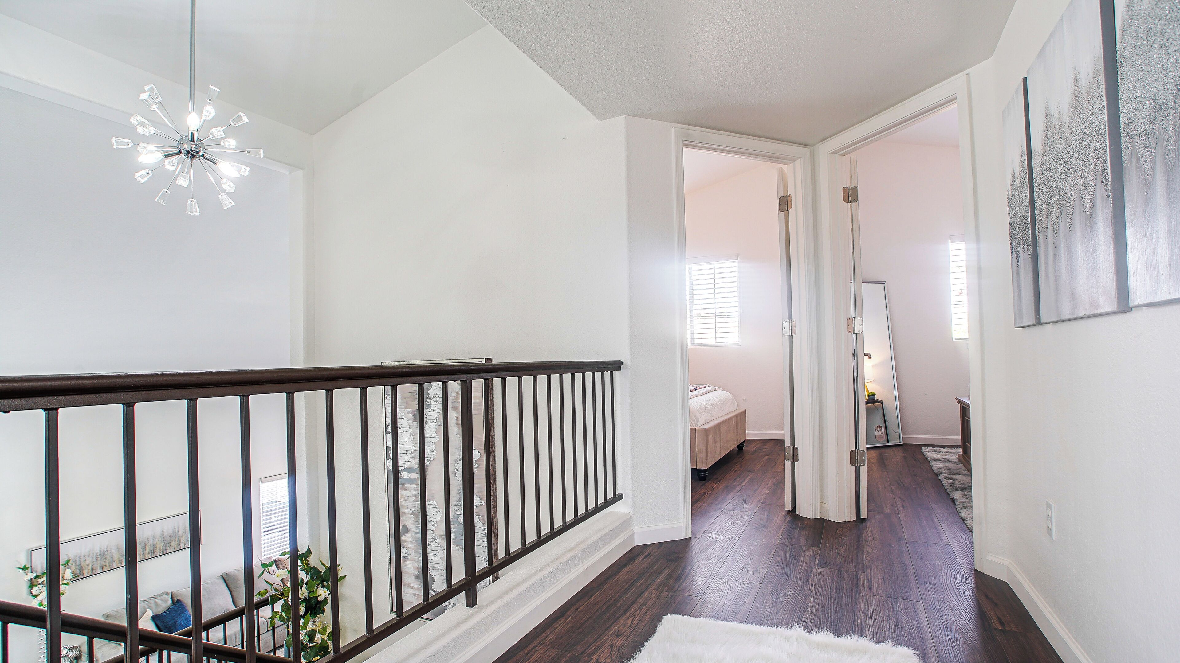 A spacious hallway with a wooden floor, a staircase with a black railing, and a ceiling light fixture.