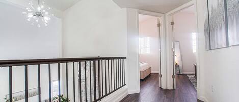 A spacious hallway with a wooden floor, a staircase with a black railing, and a ceiling light fixture.