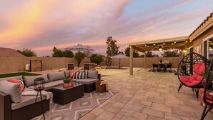 Un patio exterior con sofá, sillas, una mesa de comedor y una pérgola con luces colgantes.