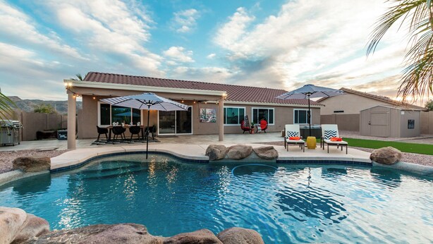 Un área de piscina residencial con terraza cubierta, mobiliario exterior y jardín ajardinado.