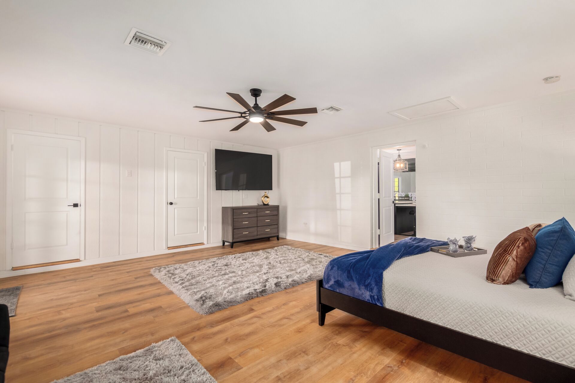 A bedroom with a bed, a ceiling fan, a TV, a dresser, and a wardrobe.