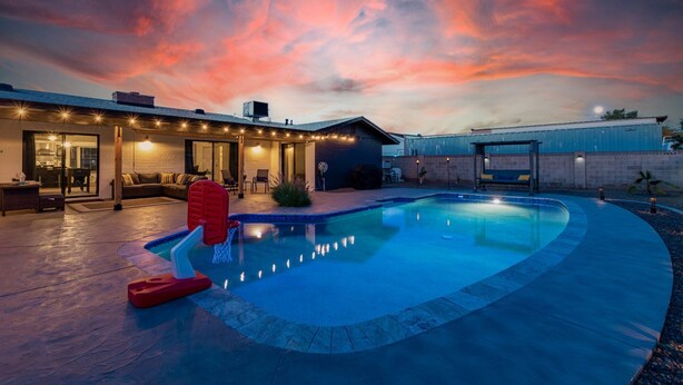 A swimming pool with a curved edge, a covered patio area with seating, and a house with a brick exterior. - Glencove Mesa (Mesa)
