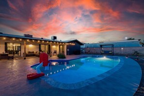 A swimming pool with a curved edge, a covered patio area with seating, and a house with a brick exterior. - Glencove Mesa (Mesa)