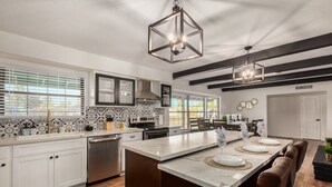 A modern kitchen with a central island, stainless steel appliances, and black-framed pendant lights. - Glencove Mesa (Mesa)