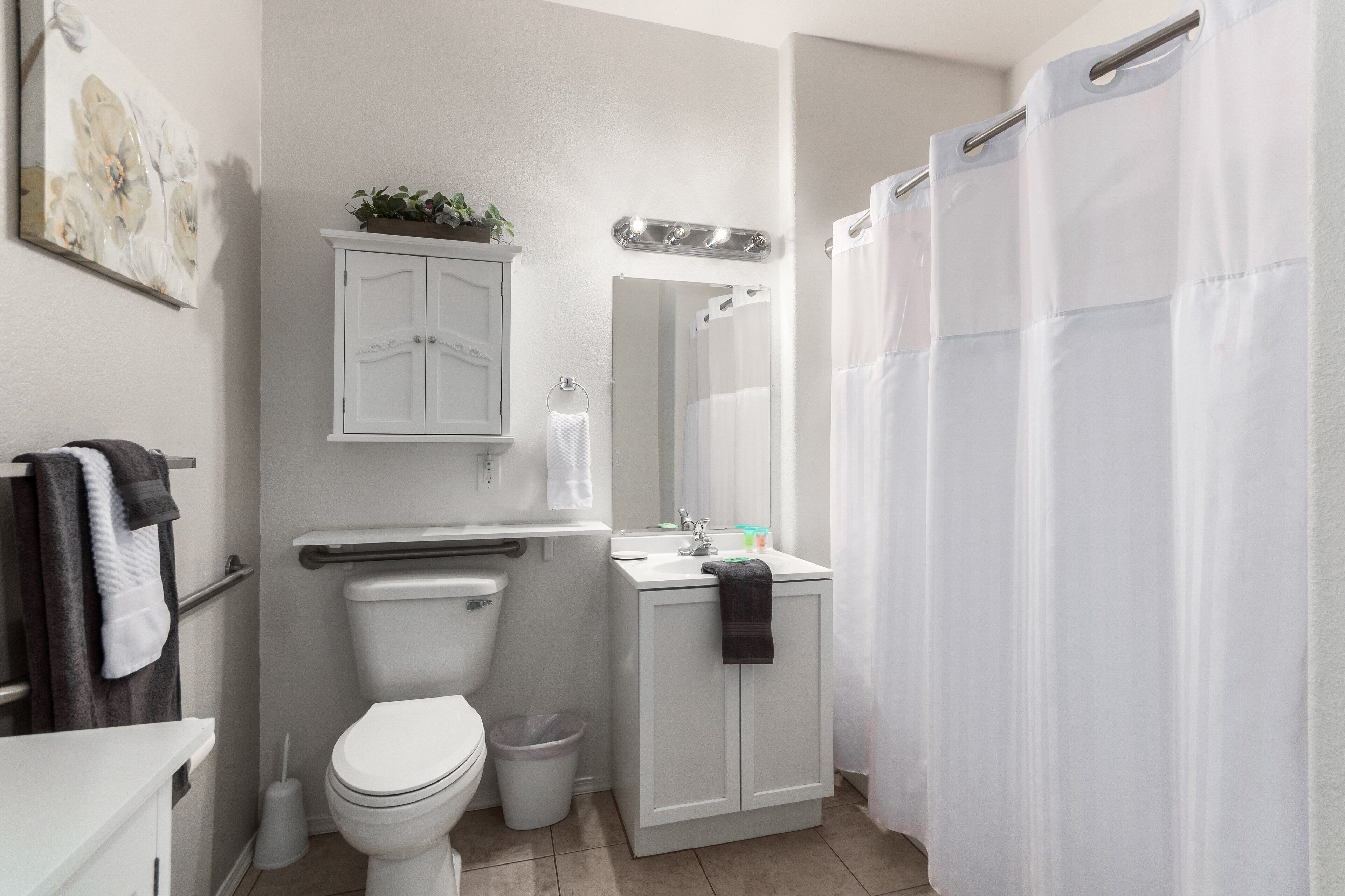 A bathroom with a toilet, sink, cabinet, and shower curtain.