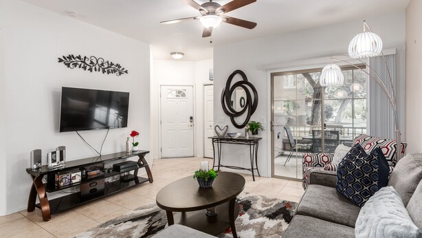 A modern living room with a flat-screen TV, a ceiling fan, a coffee table with a plant, a sofa with patterned cushions, and a dining area with a table and chairs. - Southern #1064 Mesa (Mesa)