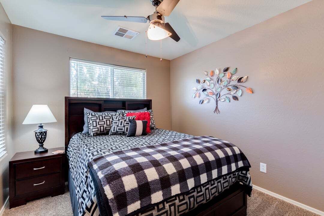 A bedroom with a bed, a nightstand, a lamp, a ceiling fan, and a wall decoration.