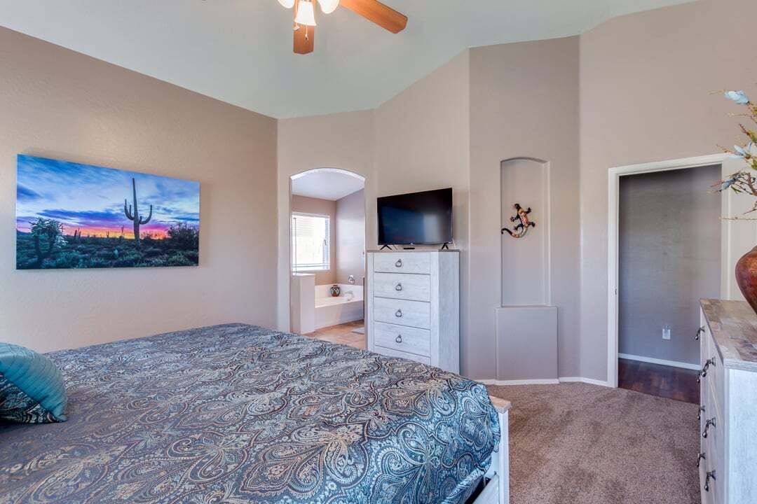 A bedroom with a bed, a television, a dresser, and a painting of a desert landscape.