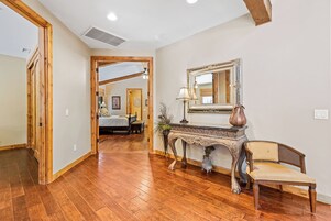 A spacious room with hardwood flooring, a wooden bench, a console table with a mirror, and a bed in the background.