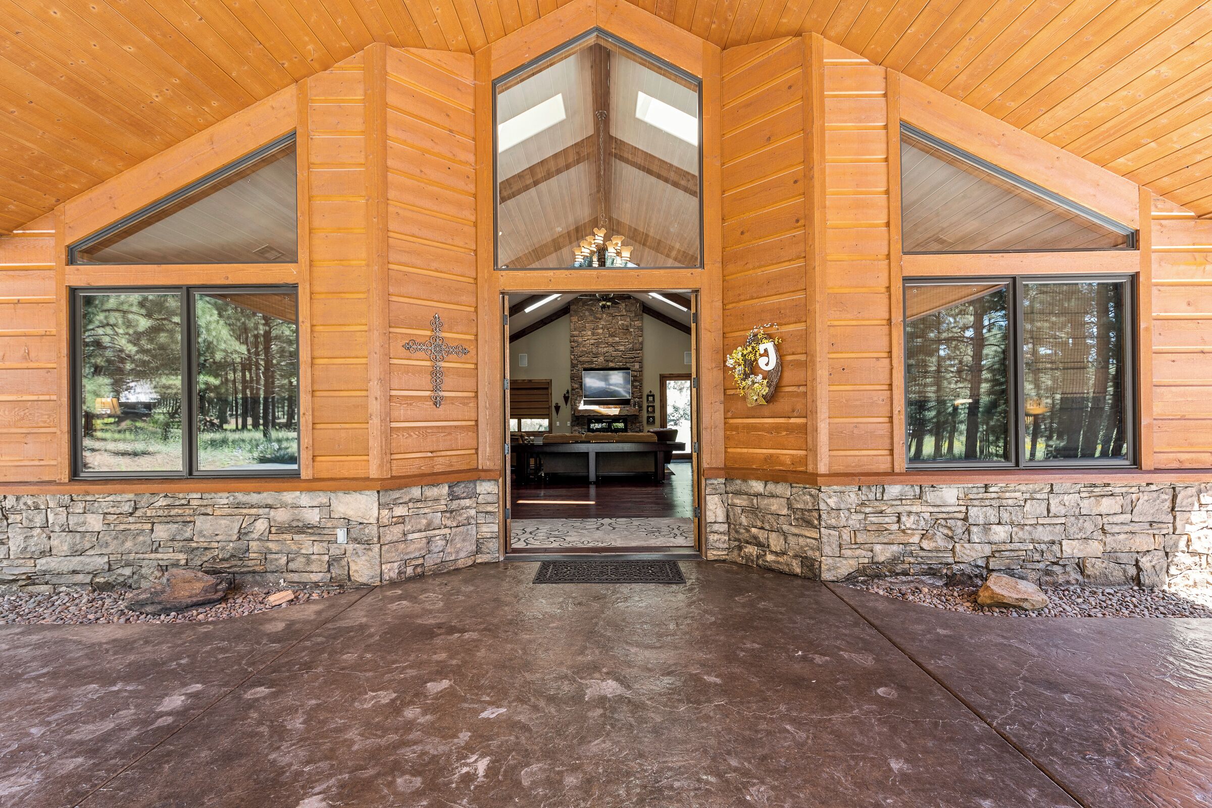 A log cabin with a stone foundation, large windows, and a stone fireplace.
