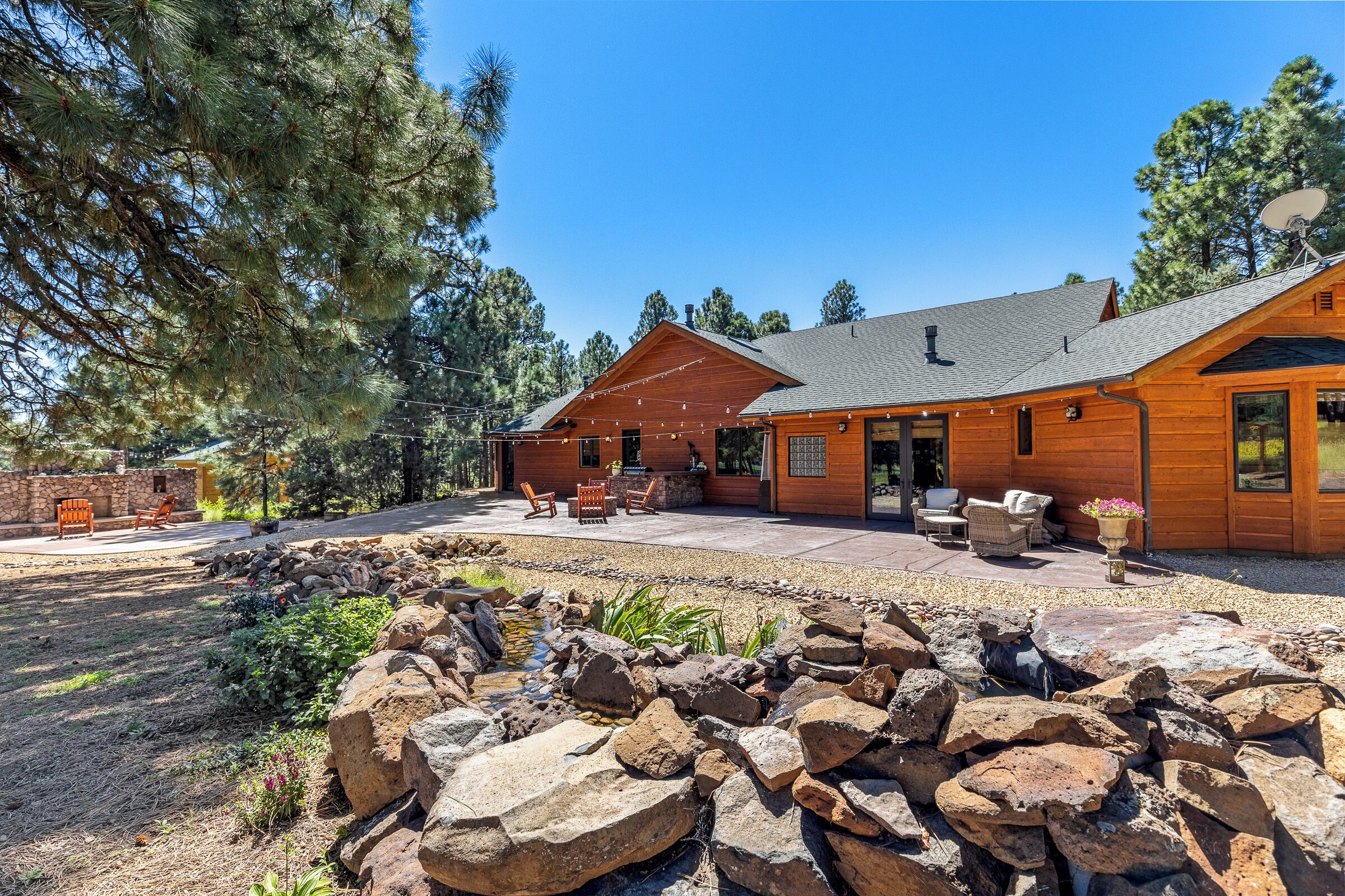 A wooden cabin with a patio area, outdoor seating, and a small pond.