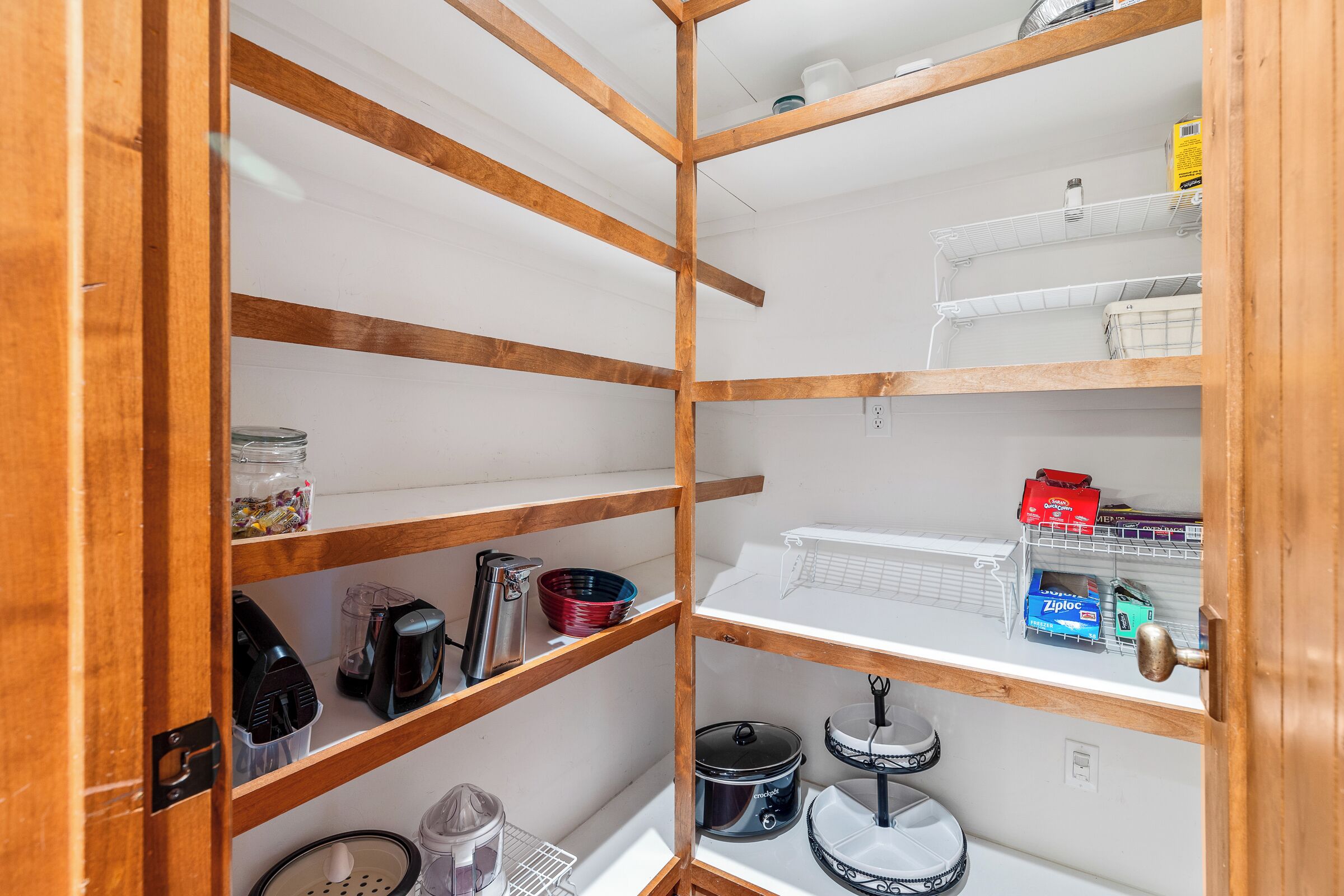 A wooden-framed storage unit with shelves, a door, and a small kitchen area with a kettle, pots, and a coffee maker.