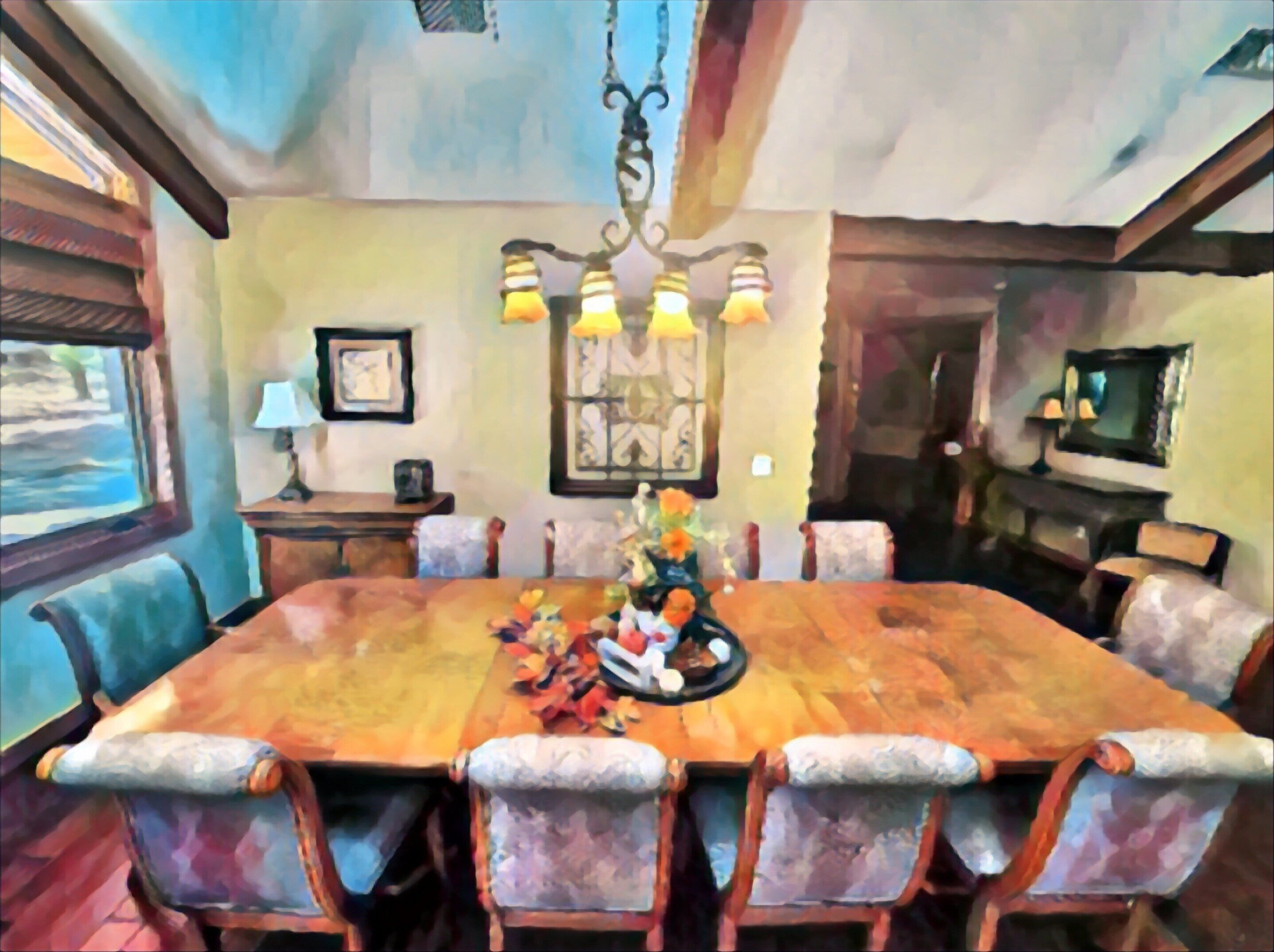 A dining room with a large wooden table surrounded by upholstered chairs, a chandelier, and a window with a view.
