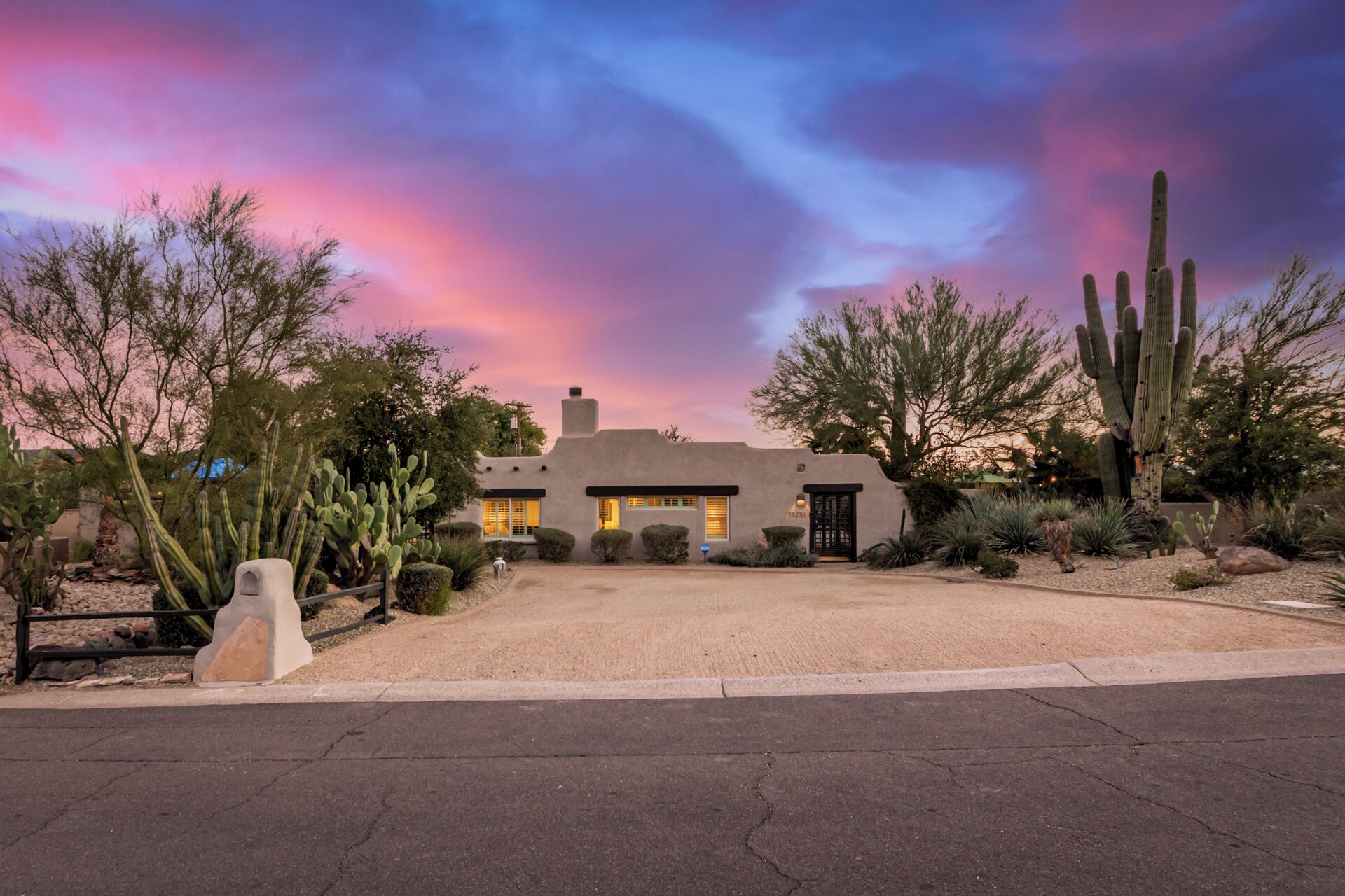 A desert-style house with a paved driveway, surrounded by cacti and desert plants.