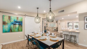 Un coin repas avec une grande table dressée pour six personnes, entourée de chaises en osier dotées de coussins bleus.