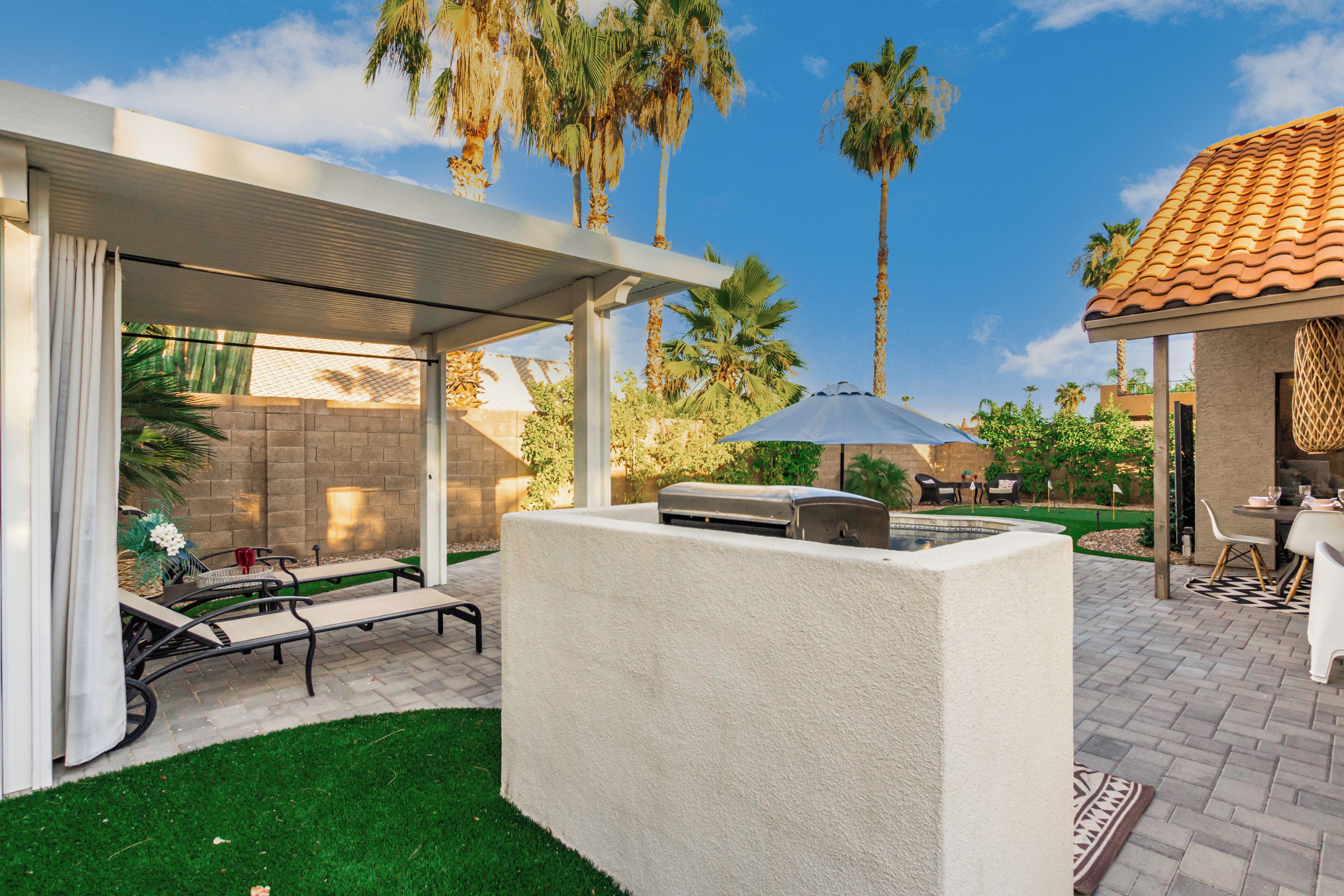 Un espace extérieur aménagé avec un barbecue, des chaises longues et un coin salon abrité.
