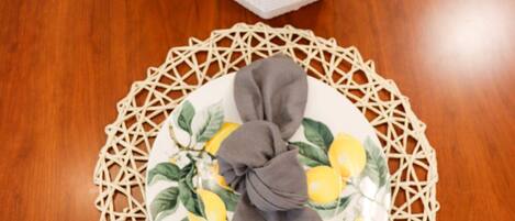 A wooden dining table with a woven placemat, a white vase with dried pampas grass, and a plate with a lemon design.